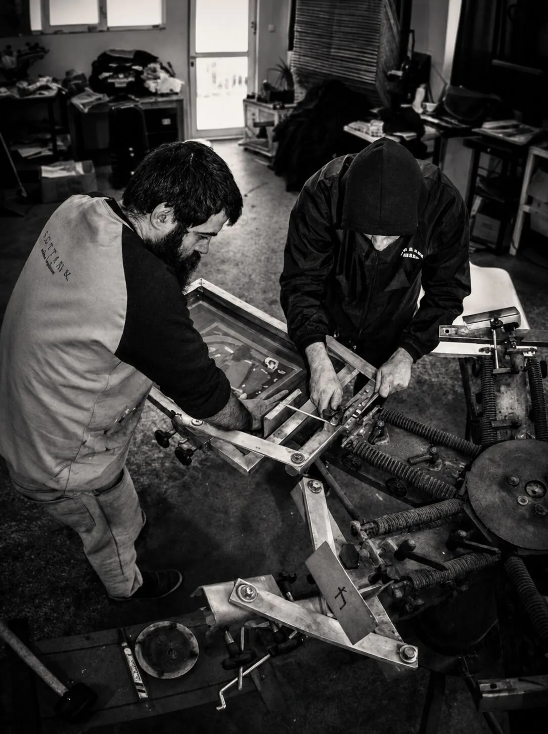 Two people preparing a screen-printing press in a workshop